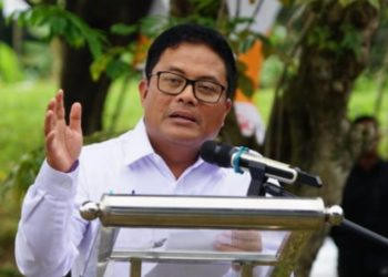 Babay Parid Wazdi berbicara di podium dengan mikrofon, mengenakan kemeja putih dan kacamata, di tengah suasana acara luar ruangan.