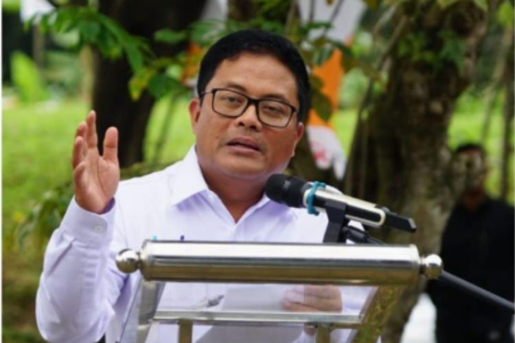 Babay Parid Wazdi berbicara di podium dengan mikrofon, mengenakan kemeja putih dan kacamata, di tengah suasana acara luar ruangan.